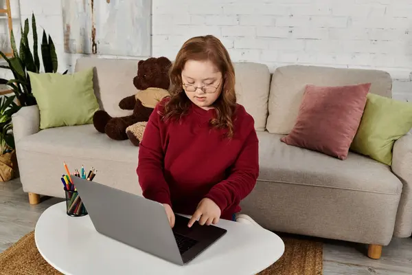 A little girl with Down syndrome uses a laptop at home. — Stock Photo