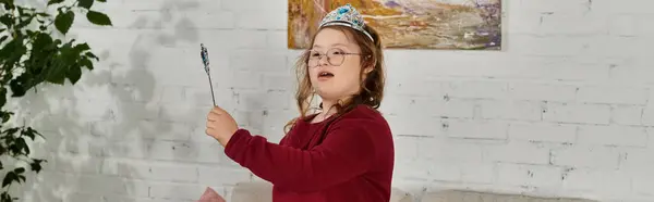 A little girl with Down syndrome plays with a wand while wearing a crown. — Stock Photo
