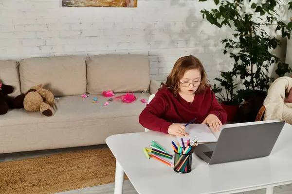 A little girl with Down syndrome sits at a table in her home, engrossed in her schoolwork. — Stock Photo