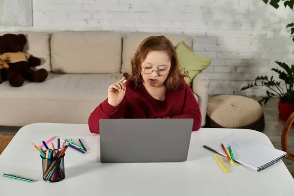 Ein kleines Mädchen mit Down-Syndrom sitzt an einem Tisch in ihrem Haus und benutzt einen Laptop. — Stockfoto