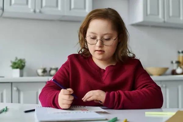 A little girl with Down syndrome sits at a table, focused on coloring with a purple pencil. — Stock Photo