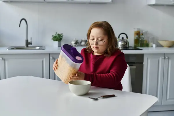 Una niña con síndrome de Down vierte cereal en un tazón en su cocina. - foto de stock