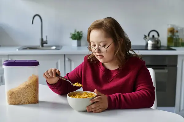 Una bambina con la sindrome di Down mangia cereali nella sua cucina. — Foto stock