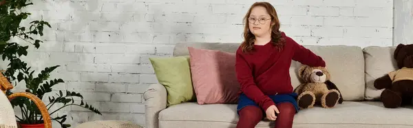 A little girl with Down syndrome sits on a couch at home. — Stock Photo