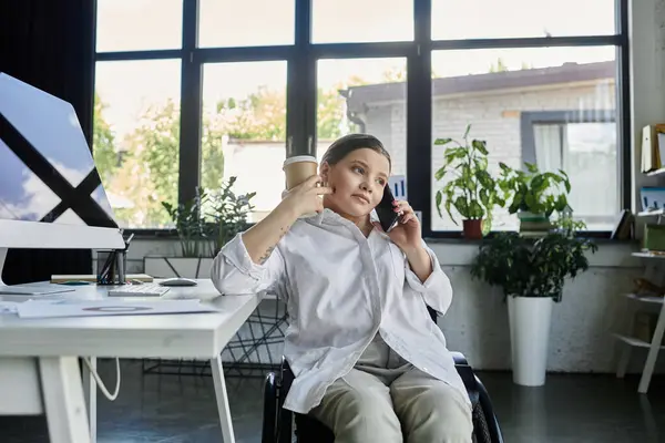 A young businesswoman in a wheelchair works at her desk in a modern office, showcasing inclusion in the workplace. — Stock Photo