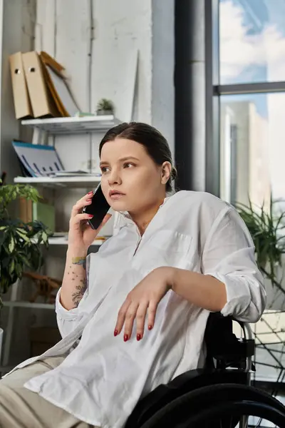 A young businesswoman in a wheelchair sits in a modern office, working on her phone. — Stock Photo