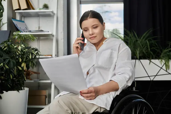 A young businesswoman in a wheelchair works on documents and talks on the phone in a modern office. — Stock Photo