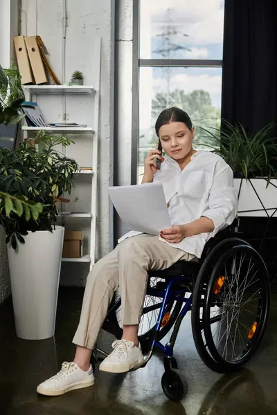 Una giovane donna d'affari si siede su una sedia a rotelle in un ufficio moderno, parlando al telefono. — Foto stock