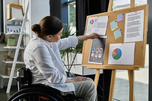 A young businesswoman in a wheelchair sits in a modern office and reviews data on a whiteboard. — Stock Photo