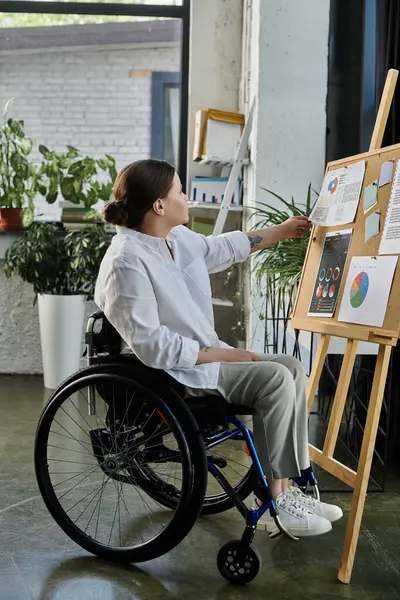 Молодая деловая женщина в инвалидной коляске сидит в современном офисе и рассматривает графики на доске. — стоковое фото