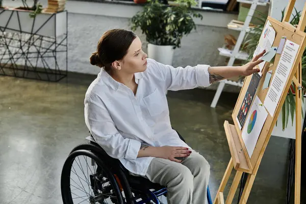 A young businesswoman in a wheelchair works at her desk in a modern office. She is focused on her work and seems confident and capable. — Stock Photo