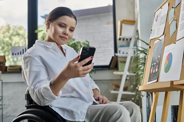 A young businesswoman in a wheelchair works on her phone in a modern office setting. — Stock Photo