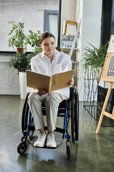 Una joven empresaria con discapacidad se sienta en su silla de ruedas y examina cuidadosamente los documentos en un entorno de oficina moderno. - foto de stock