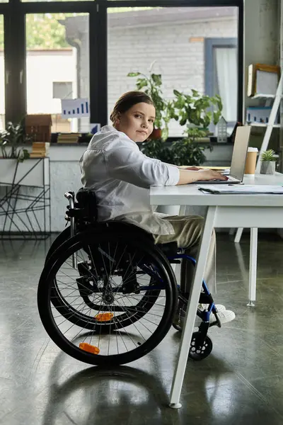 A young businesswoman in a wheelchair works at a desk in a modern office setting. — Stock Photo
