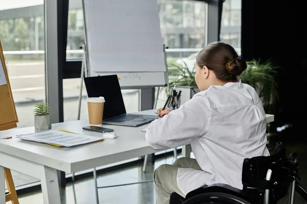 A young businesswoman with a disability sits in a wheelchair, working at a desk in a modern office. — Stock Photo