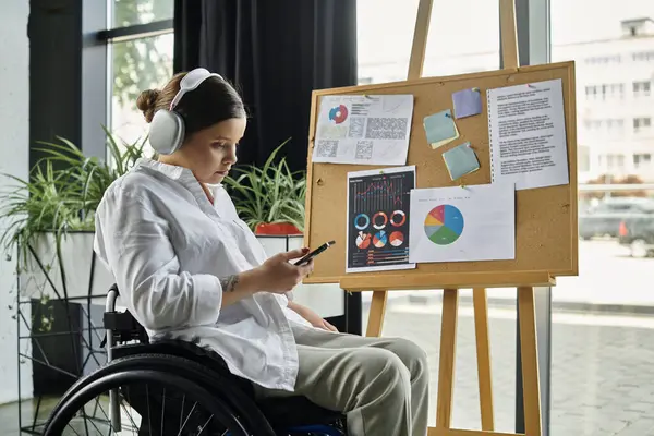 A young businesswoman, sitting in a wheelchair, works on a project in a modern office setting. — Stock Photo