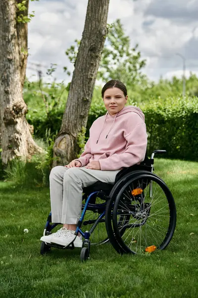 A young woman with a disability sits in her wheelchair, enjoying a peaceful moment in a green park. — Stock Photo