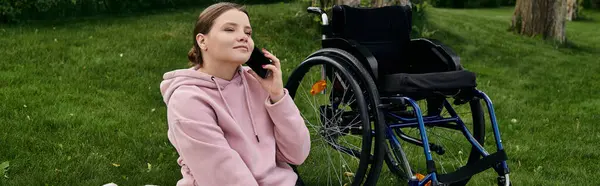 A young woman with a disability sits in her wheelchair, enjoying a moment of peace in a green park, as she talks on her phone. — Stock Photo