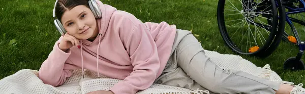 Eine junge Frau im rosafarbenen Kapuzenpullover entspannt sich auf einer Decke im Gras, ihr Rollstuhl in der Nähe. — Stockfoto