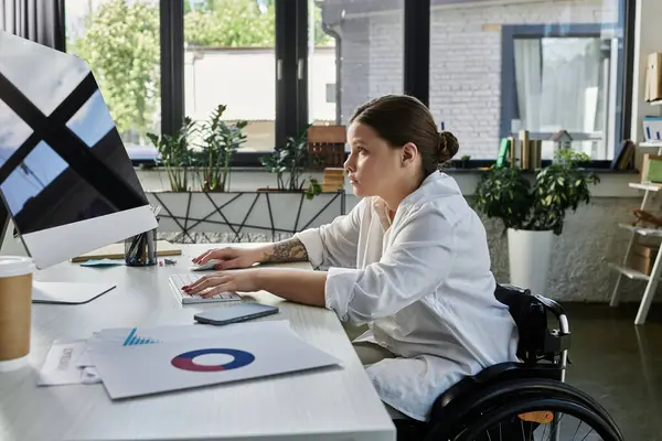 A young businesswoman in a wheelchair works on a computer in a modern office setting. — Stock Photo