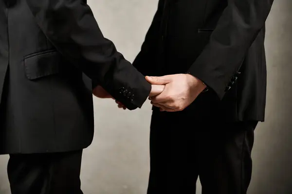Zwei Männer in passenden schwarzen Anzügen halten Händchen und zeigen ihre Liebe und ihren Stil. — Stockfoto