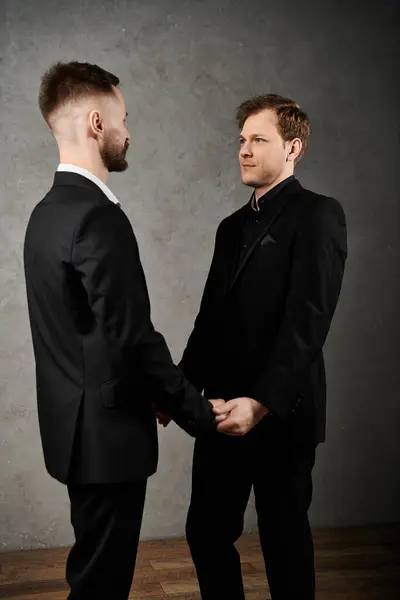 Two men in elegant suits stand close together, their hands intertwined, exchanging a tender glance. — Stock Photo