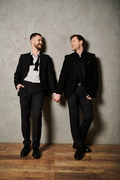 Two men in black suits stand close, smiling and holding hands. — Stock Photo