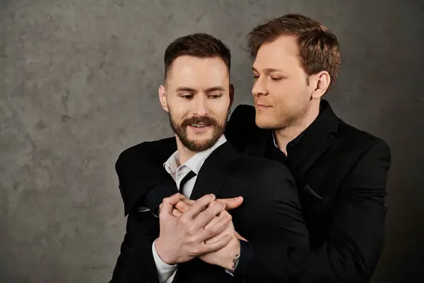 Two men in elegant suits embrace against a grey background. — Stock Photo