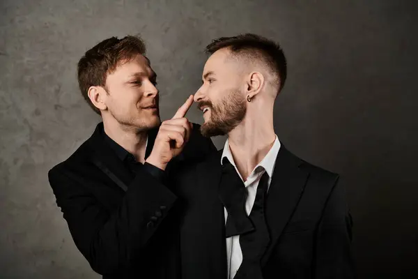 Dois homens em ternos elegantes interagem brincando contra um pano de fundo cinza. — Fotografia de Stock