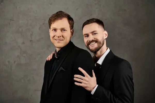A loving gay couple poses in elegant suits against a gray backdrop. — Stock Photo