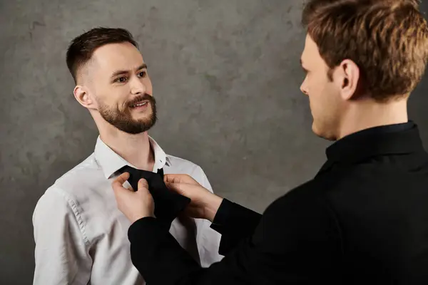 Two men, dressed in elegant suits, stand close together. One man is fixing the bow tie of the other. — Stock Photo