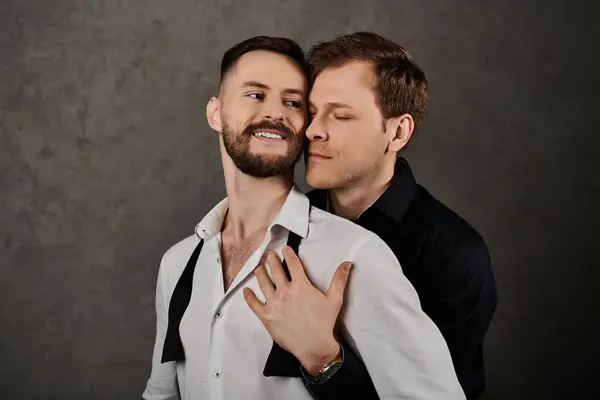 Двое мужчин в элегантных костюмах стоят рядом, один обнимает другого нежным выражением лица. — стоковое фото