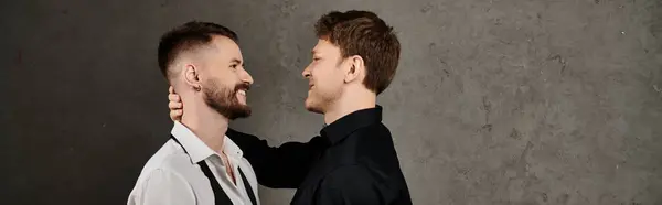 Two men, dressed in elegant suits, share a loving embrace in front of a grey wall. — Stock Photo
