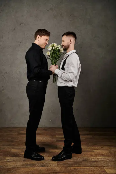 Two men in elegant suits exchange a loving glance and a bouquet of white flowers. — Stock Photo