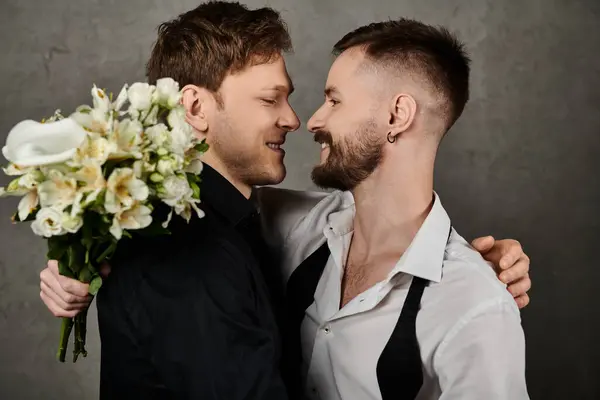 Zwei Männer in eleganten Anzügen teilen einen liebevollen Moment, einer hält einen Strauß weißer Blumen in der Hand. — Stockfoto