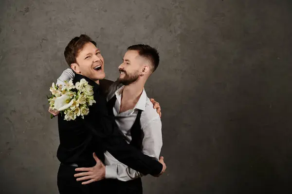 Zwei Männer in Anzügen umarmen sich, einer hält einen Strauß weißer Blumen in der Hand, beide lachen. — Stockfoto