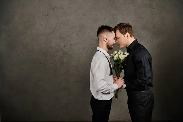 A gay couple in suits touch foreheads while sharing a bouquet of white flowers. — Stock Photo