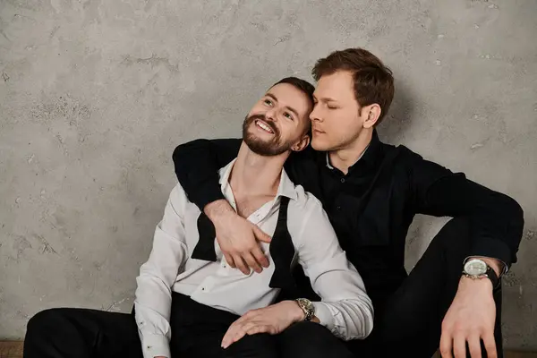 Zwei Männer in eleganten Anzügen teilen einen zarten Moment gegen eine Betonwand. — Stockfoto