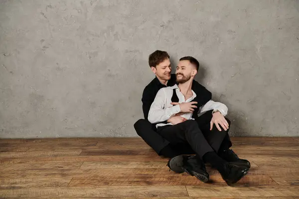 A loving gay couple in elegant suits embrace and share a tender moment against a concrete backdrop. — Stock Photo