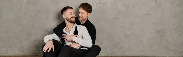Two men in elegant suits share a loving embrace against a concrete backdrop. — Stock Photo