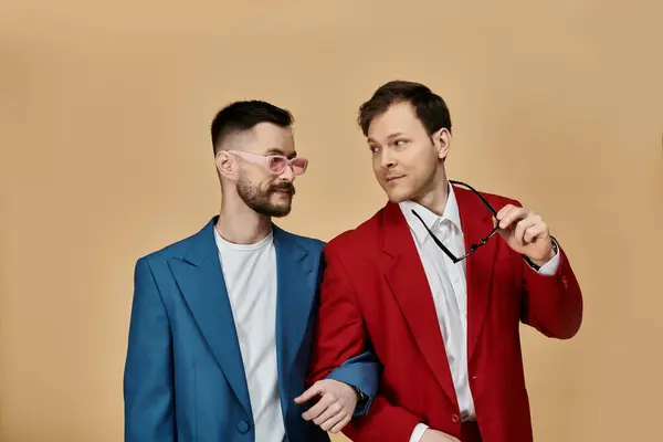 Two men in suits, one in blue and one in red, stand close together against a tan backdrop. — Stock Photo