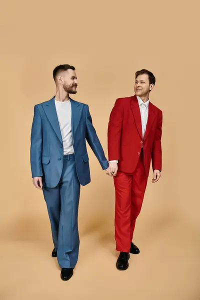 Two men in elegant suits walk hand-in-hand, showcasing a vibrant blue and red color combination. — Stock Photo