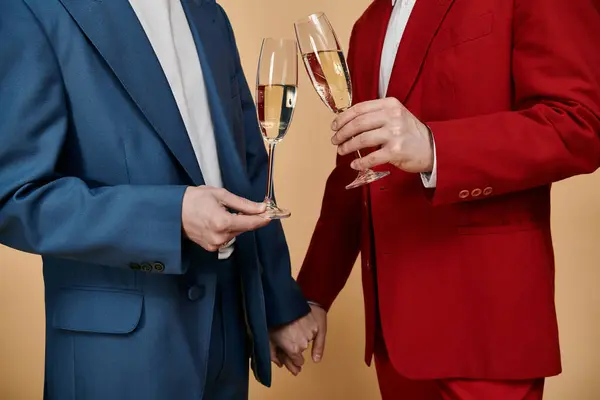 Два чоловіки в костюмах, один синій і один червоний, піднімають свої флейти шампанського в святковому тості. — стокове фото