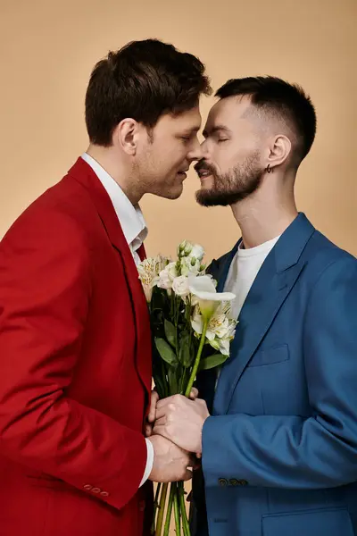 Two men in elegant suits share a loving moment, holding a bouquet of white flowers. — Stock Photo