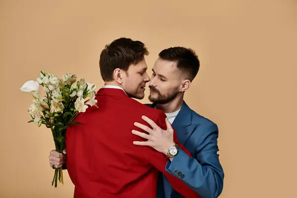 Deux hommes en costume de dapper embrassent, l'un tenant un bouquet de fleurs blanches. — Photo de stock