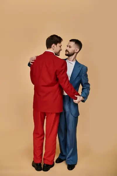 Two men in suits, one red and one blue, stand close together and look at each other with love. — Stock Photo