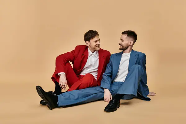Two men in stylish suits sit on the floor, smiling and looking at each other. — Stock Photo
