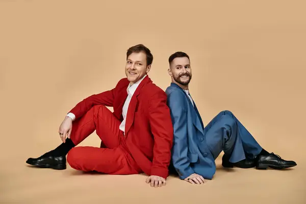 Two men in elegant suits sit back to back, embracing each other with joy and affection. — Stock Photo