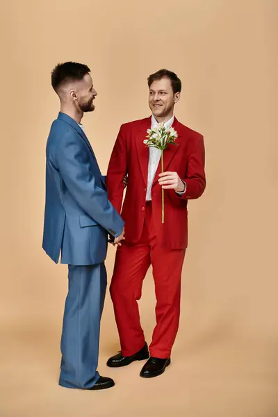 Una coppia gay in abiti eleganti stare vicino insieme, uno presentando fiori all'altro. — Foto stock