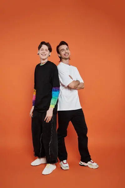Two young friends in stylish clothing pose against an orange background. — Stock Photo